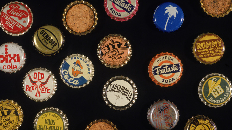 An old collection of metal bottle caps is being displayed on a black backdrop.
