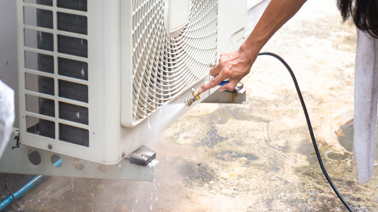 A person cleaning an air conditioner with a hose