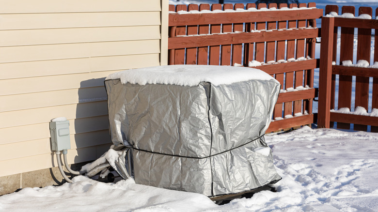 An AC unit with a cover on it in the snow