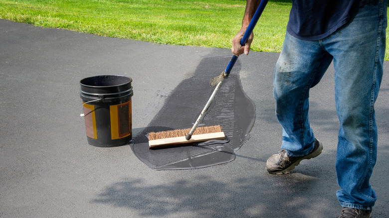 man spreading sealant on asphalt driveway