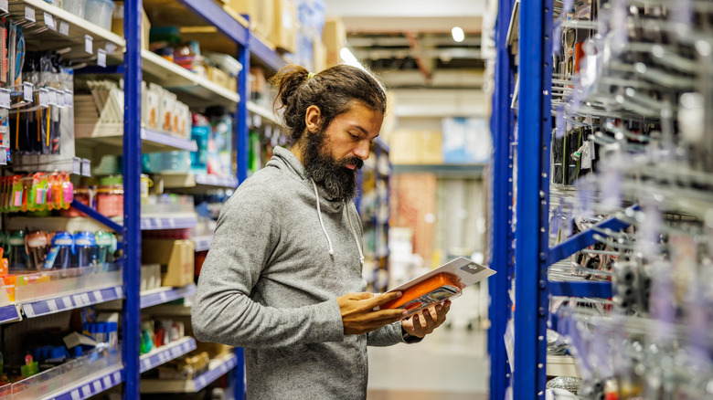 A man looks carefully at an item while standing in an aisle of a hardware store