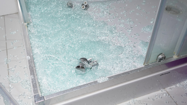 Broken glass shower door with chrome handle on the tiled floor of a bathroom