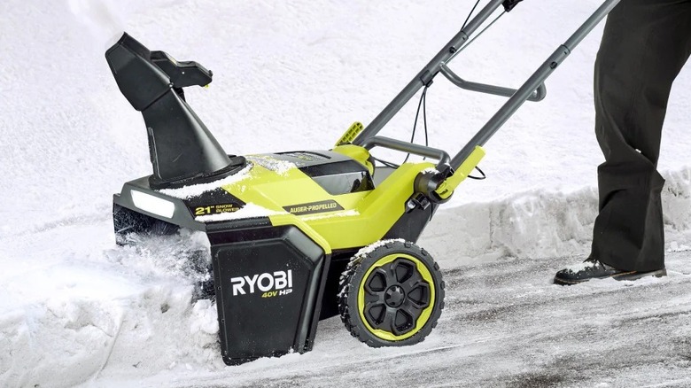 Person using a Ryobi snow blower on a driveway