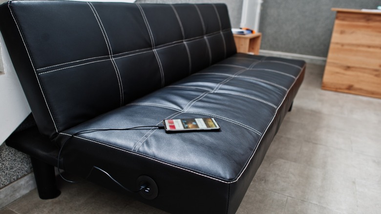 A smartphone plugged into a sofa's USB charging station
