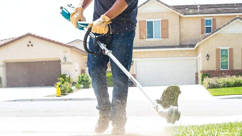 Man using a Makita string trimmer near a sidewalk