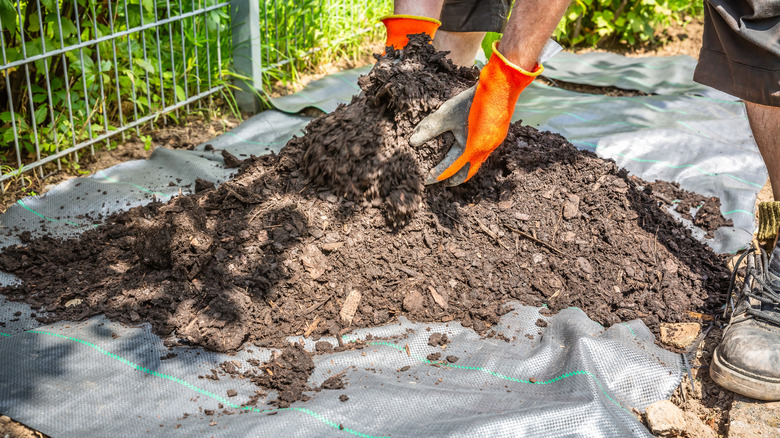A person in orange gardening gloves placing mulch on top of black landscape fabric in a garden