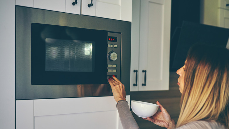 Woman with a white bowl in her hand setting microwave,