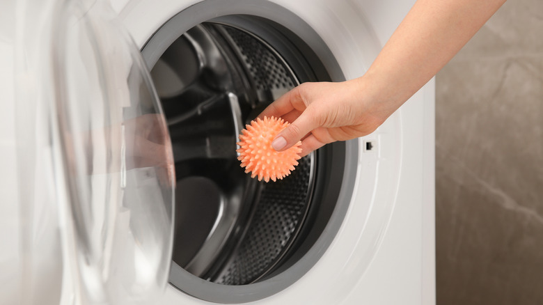Hand putting an orange dryer ball in the dryer
