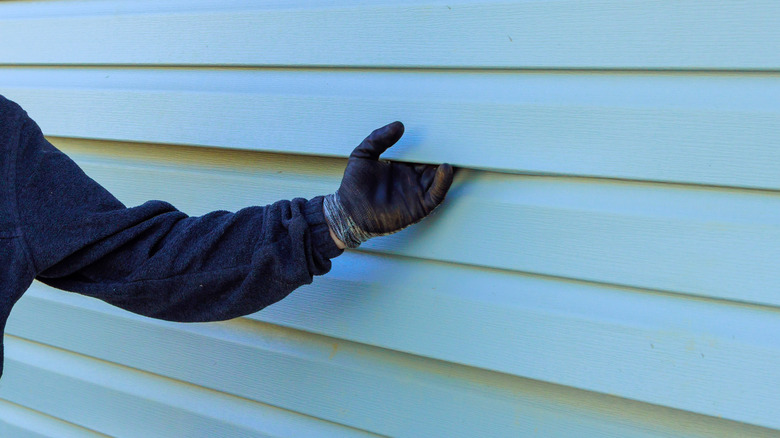 Gloved worker gripping panel of vinyl siding on a home