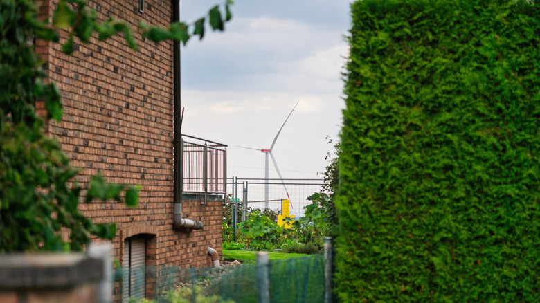 A wind turbine can can be seen near the yard of a brick building