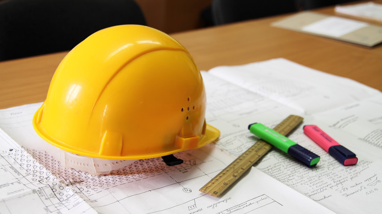 Yellow hard hat, ruler, and markers on top of building plans on a desk