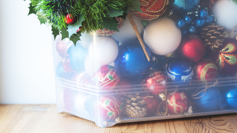 Blue, red, and white Christmas tree ornaments in clear plastic bin on wood floor