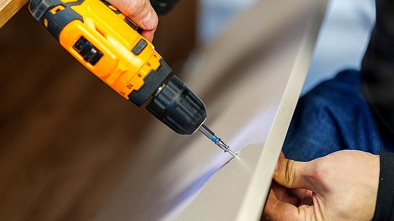 Close-up of a person using a drill to add a screw into a piece of furniture