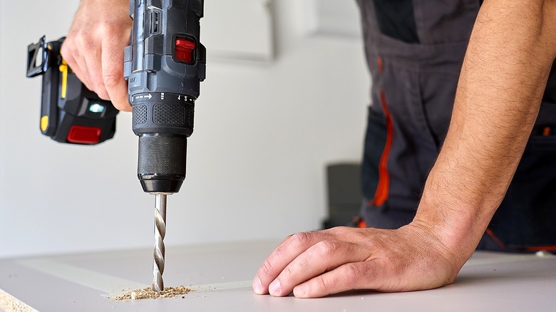 Person drilling into a plank of engineered wood