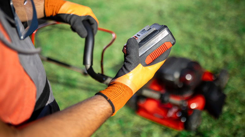 person standing in lawn holding battery of battery-powered mower