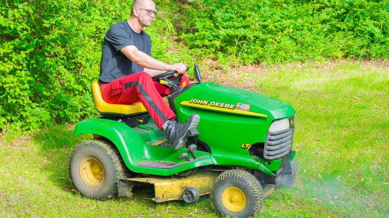 man cutting grass with green lawn tractor