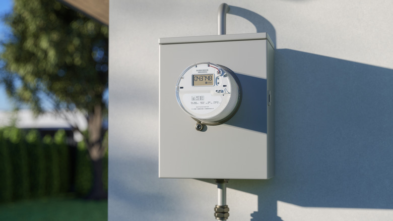 An electric meter is shown on the side of a gray house