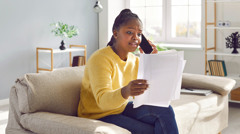 A woman talks on the phone while looking at a bill