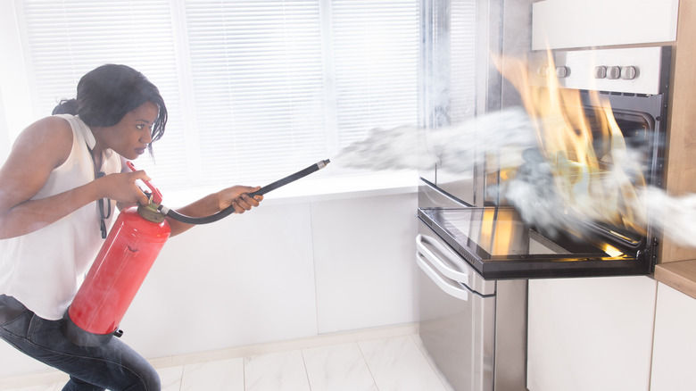 woman pointing fire extinguisher at oven