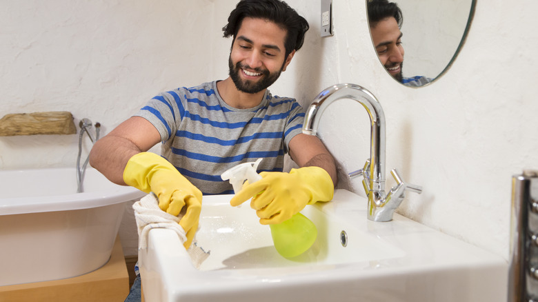 man with spray bottle cleaning sink