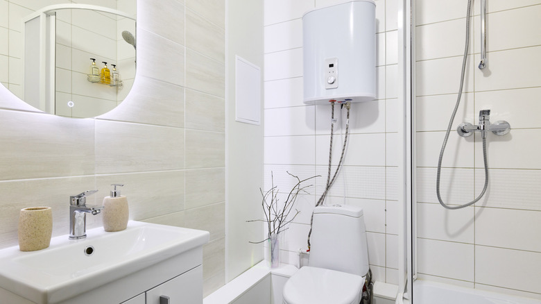 A bathroom with an above-toilet tank, a small shower, and an illuminated mirror