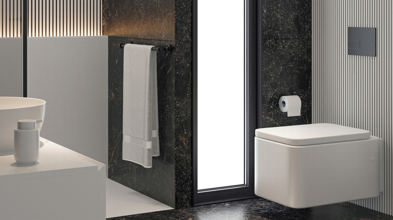 A floating square toilet with a shower blocked by a wall and lots of illumination