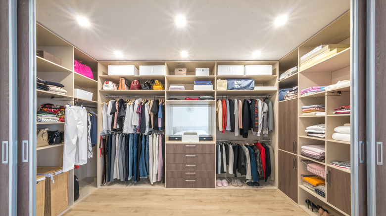 A large walk-in closet with hanging rods, shelves with storage bins, and drawers filled with hanging and folded clothing