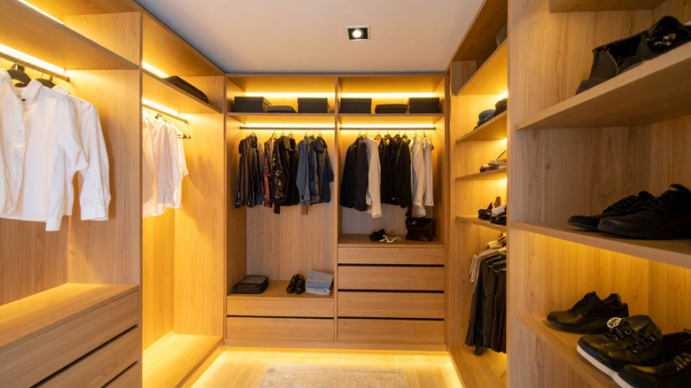 A fancy walk-in closet with wood shelving and drawers highlighted by lighting throughout