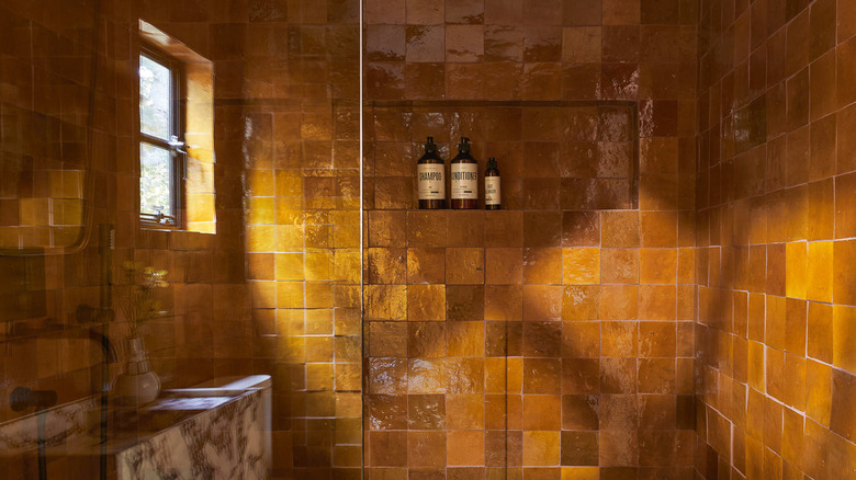 A bathroom shower covered in amber-colored tiles in slightly different shades