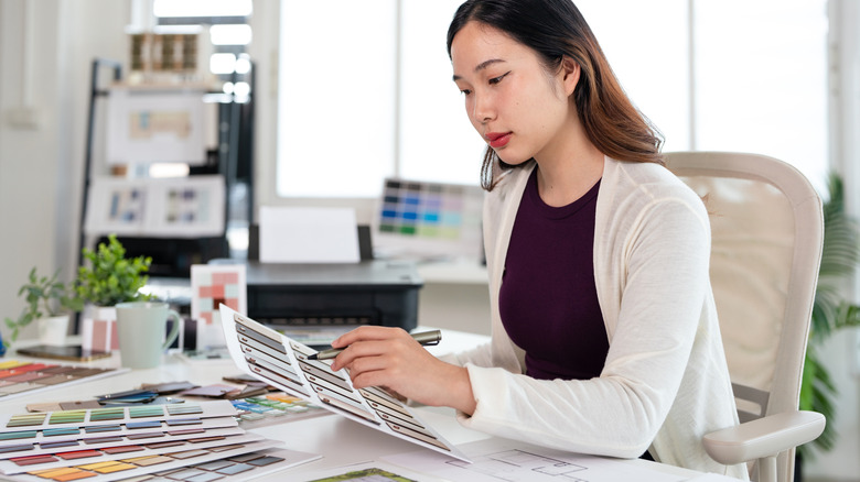 A woman sitting at a desk choosing paint colors from a swatch selection.