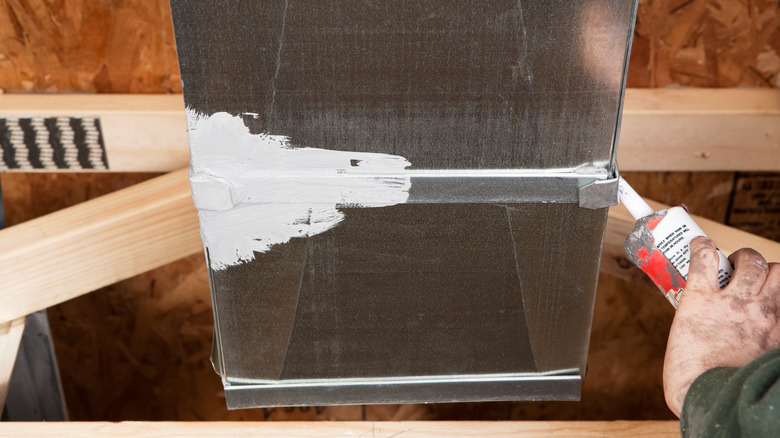 Person sealing ducts with caulk