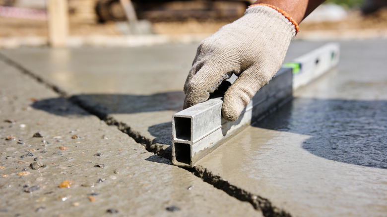 A gloved hand smooths out freshly poured concrete on a sunny day.
