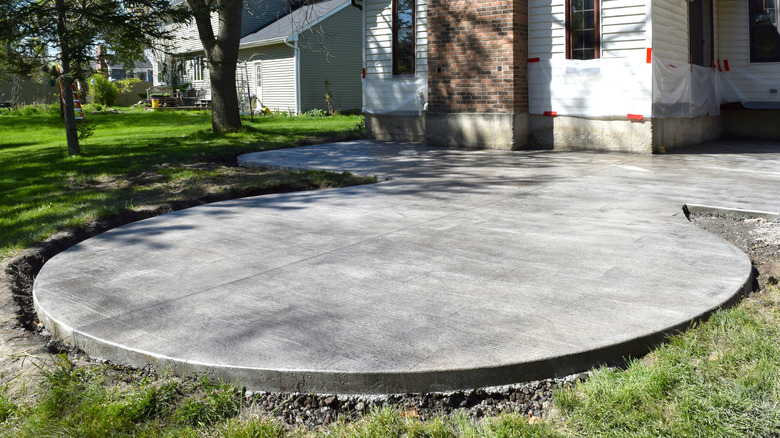 A newly installed circular concrete patio in a yard with trees and a house in the background.