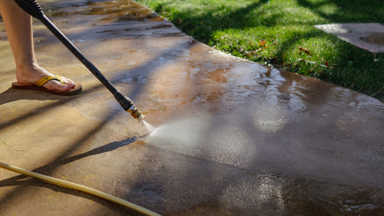 A person uses a pressure washer to clean a concrete patio.