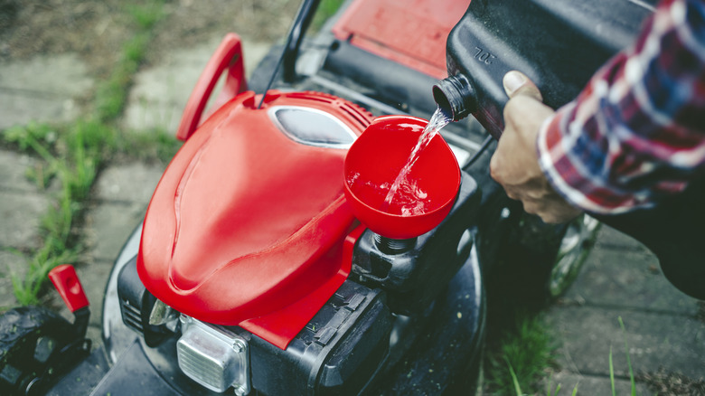 A man pouring fuel into the tank of a gas-powered lawn mower