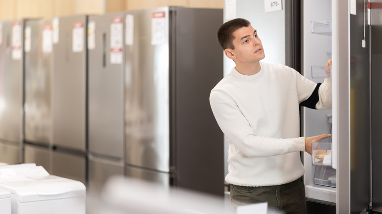 A guy shopping for a refrigerator in a home appliance store.