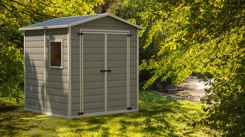 A plastic storage shed surrounded by trees in a grassy area