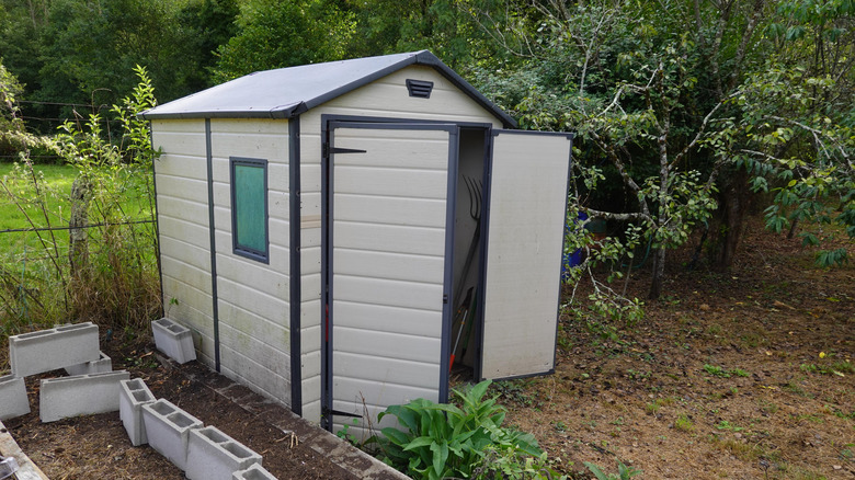 A plastic storage shed with an open door and garden tools inside