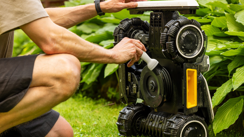 Man cleaning the underside of a robot lawn mower