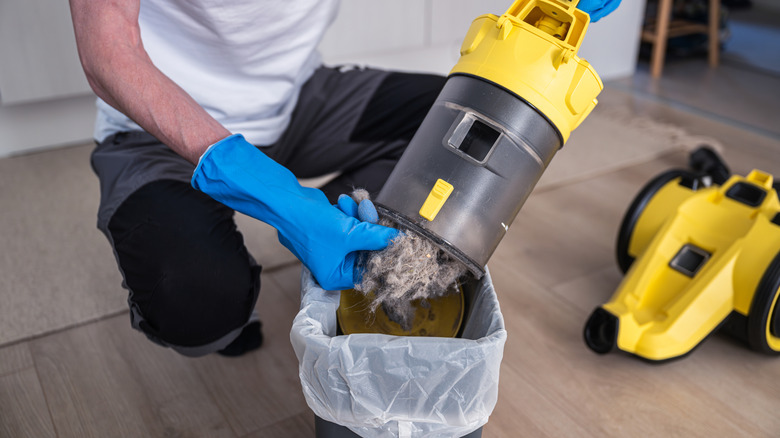 A person with blue cleaning gloves emptying out a canister from a vacuum cleaner.