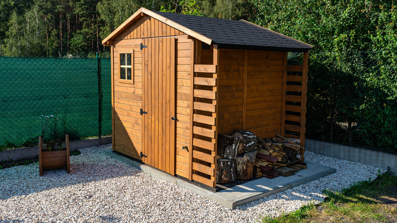 A wooden garden shed standing on a concrete foundation in a garden.