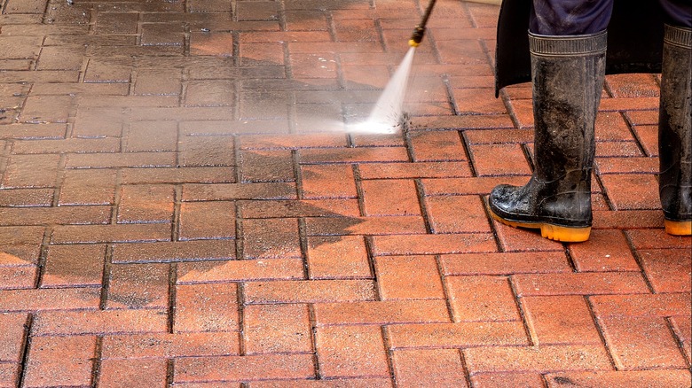 Close-up on a person power-washing brick pavers