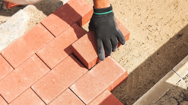 A gloved hand lays red bricks as pavers for a building project