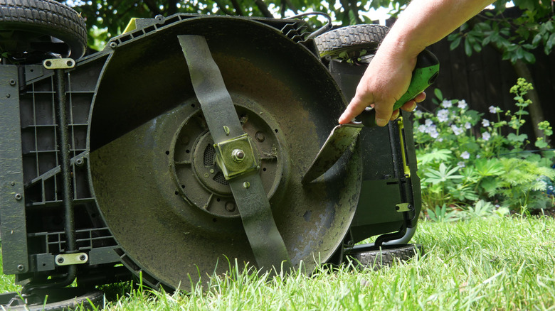 A person cleaning the underside of their push mower