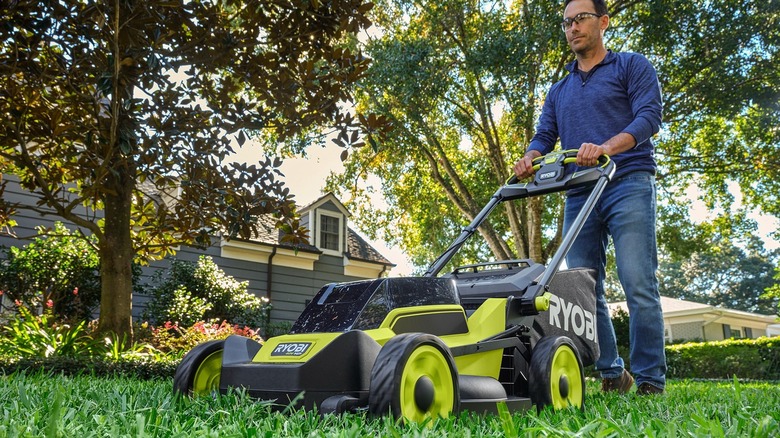 A person mowing their lawn with a Ryobi walk-behind push mower