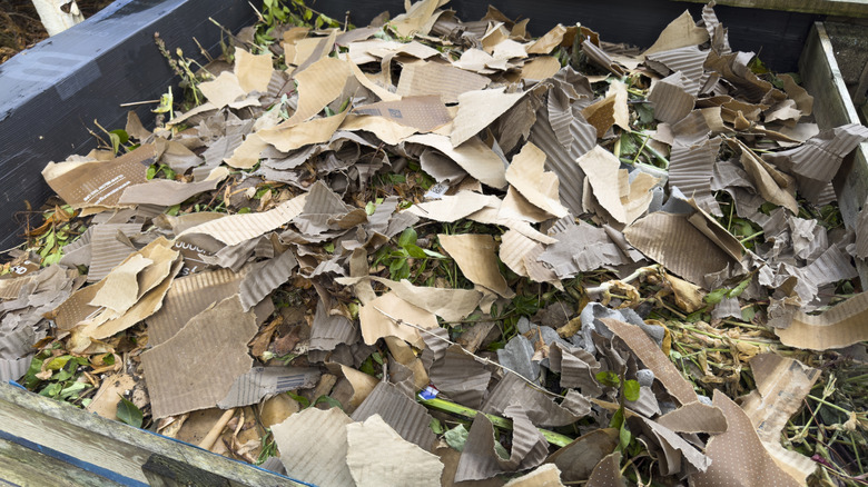 A compost pile with brown materials on top and some green materials peeking through.