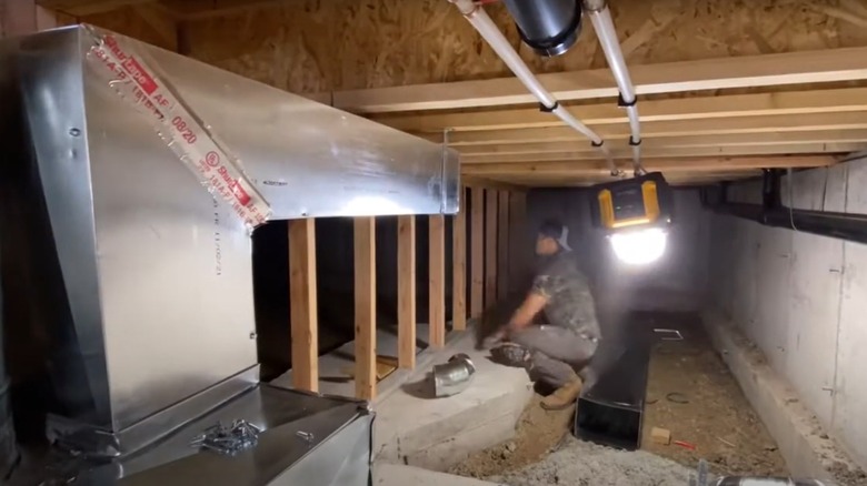 Man installing HVAC ductwork inside a crawl space