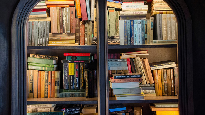 A dark wood bookcase with books piled up behind its glass doors