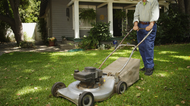 An older person pushing a lawn mower in the front yard