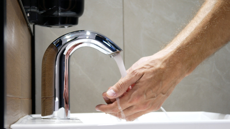 A side view of a man's hands held under the running water of a silver faucet